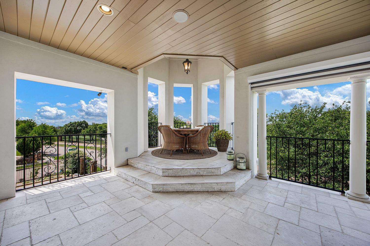 A modern covered porch with white stone flooring, wooden ceiling, and panoramic views of the surrounding landscape.