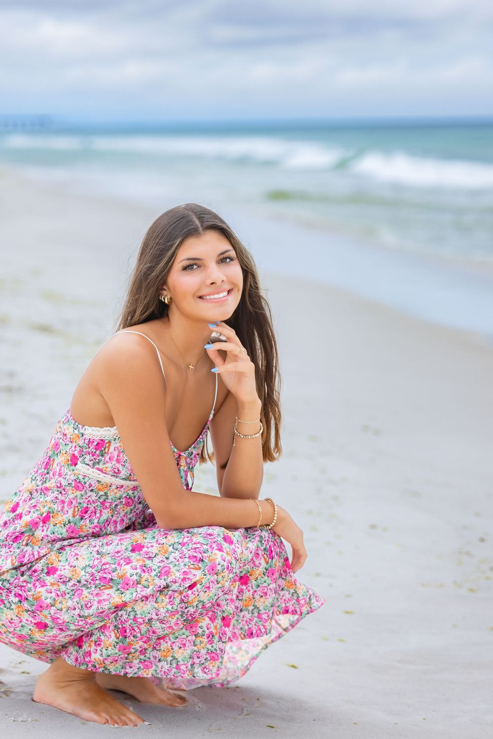 Woman in floral dress laying on white sandy beach with ocean waves and blue sky in background.