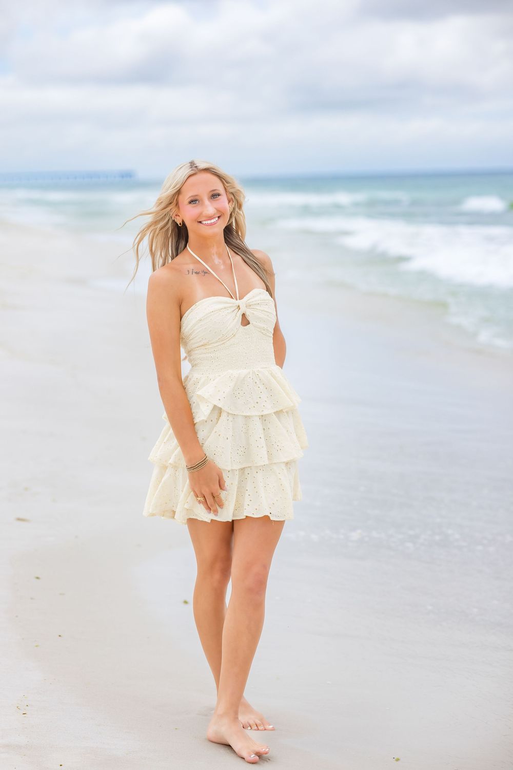 A whimsical beach photo shoot featuring a cream-colored ruffled romper against the ocean waves and sandy shoreline.