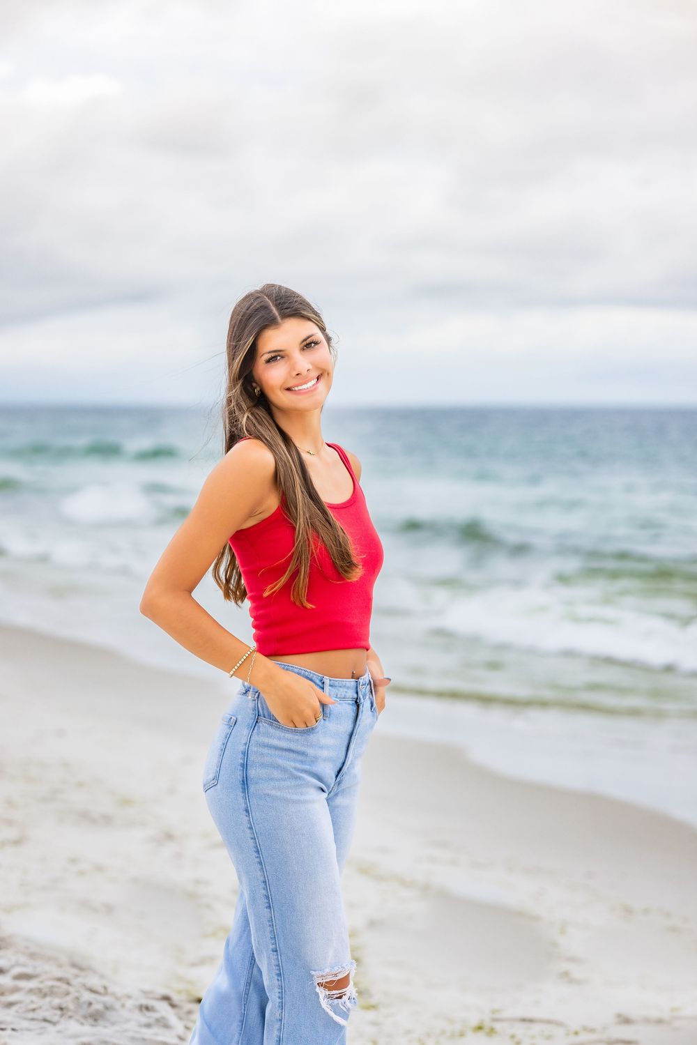Casual beach portraits featuring denim jeans and a red top with the ocean waves creating a serene backdrop.