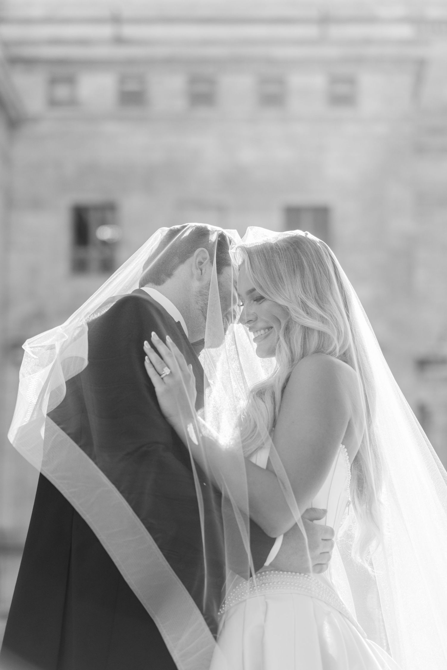 Romantic wedding photograph on sunny lawn with grand neoclassical columns and architecture in the background.