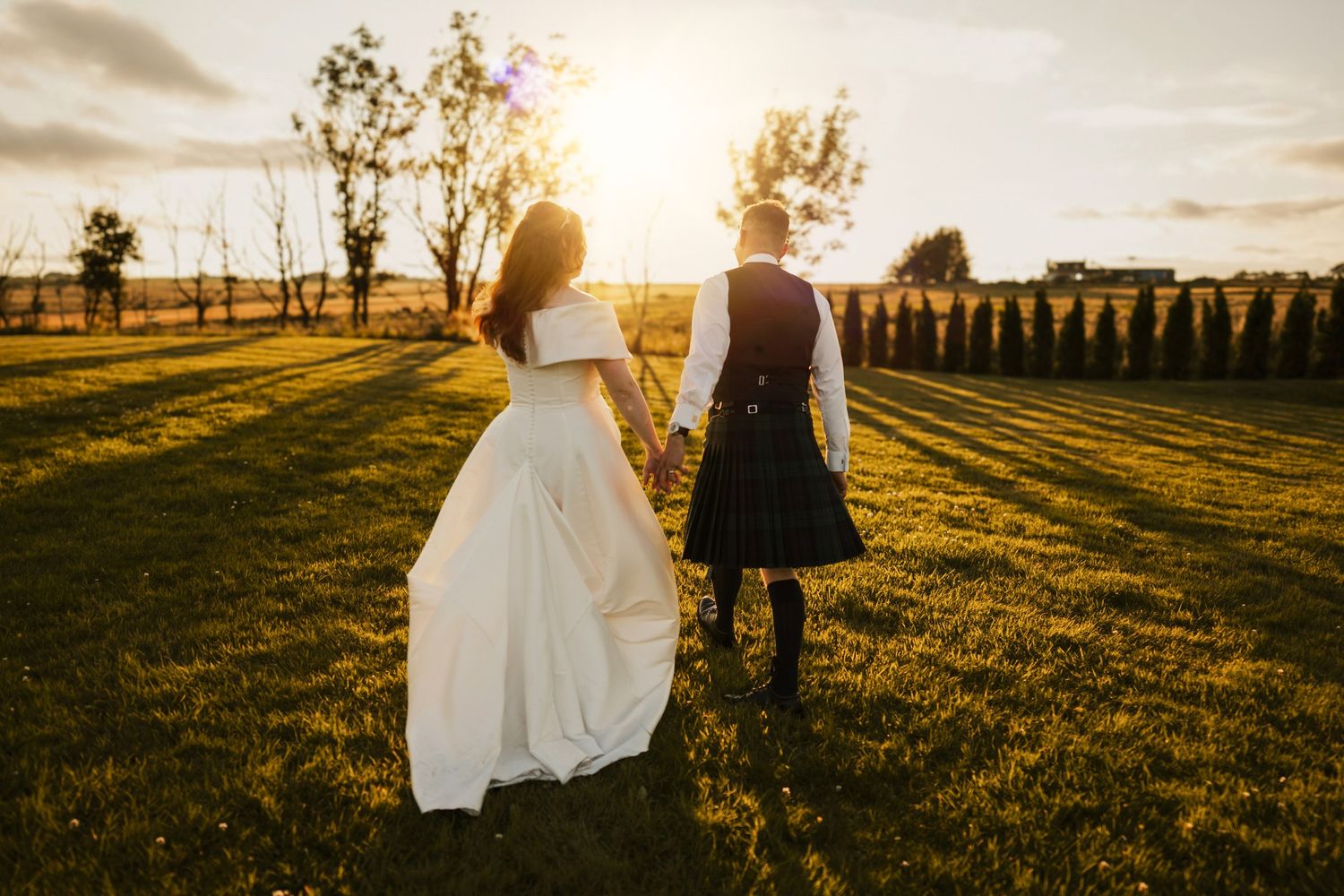 A couple in wedding attire stands intimately on an industrial staircase by large windows with dramatic lighting.