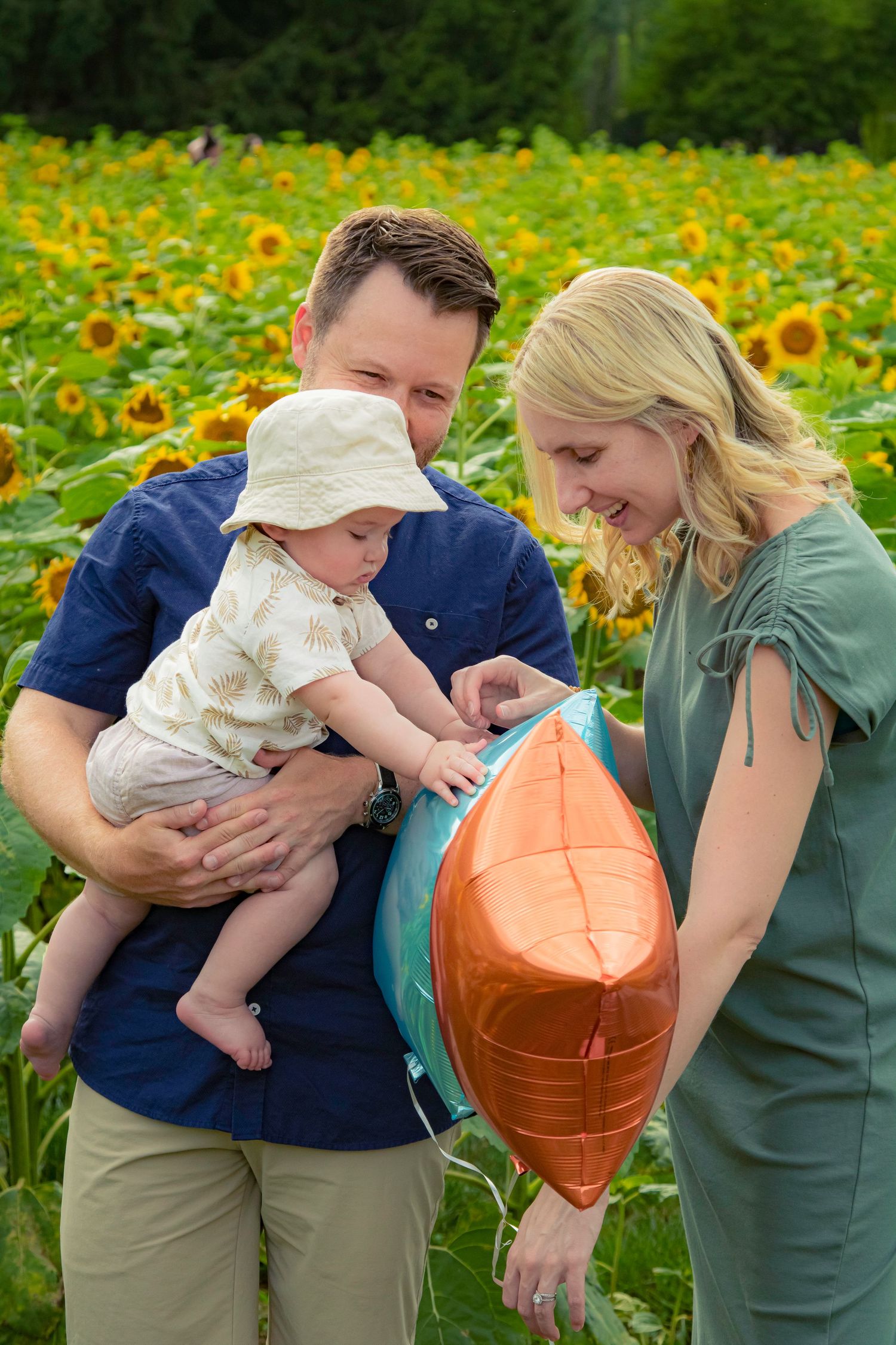Family enjoying a moment together in a sunflower field, with a child touching an orange balloon held by adults.