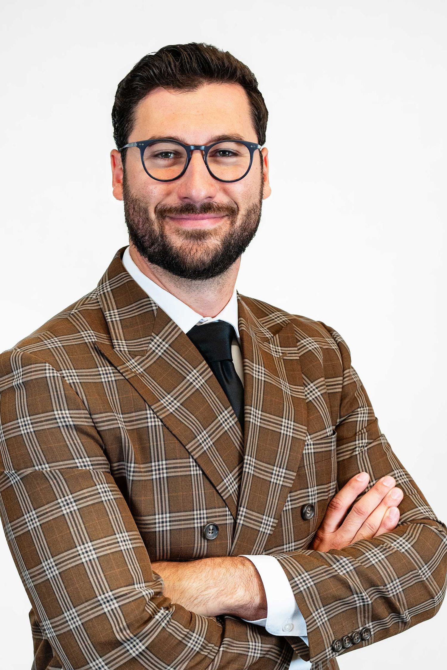 Professional wearing brown plaid blazer and glasses poses with crossed arms against white background.