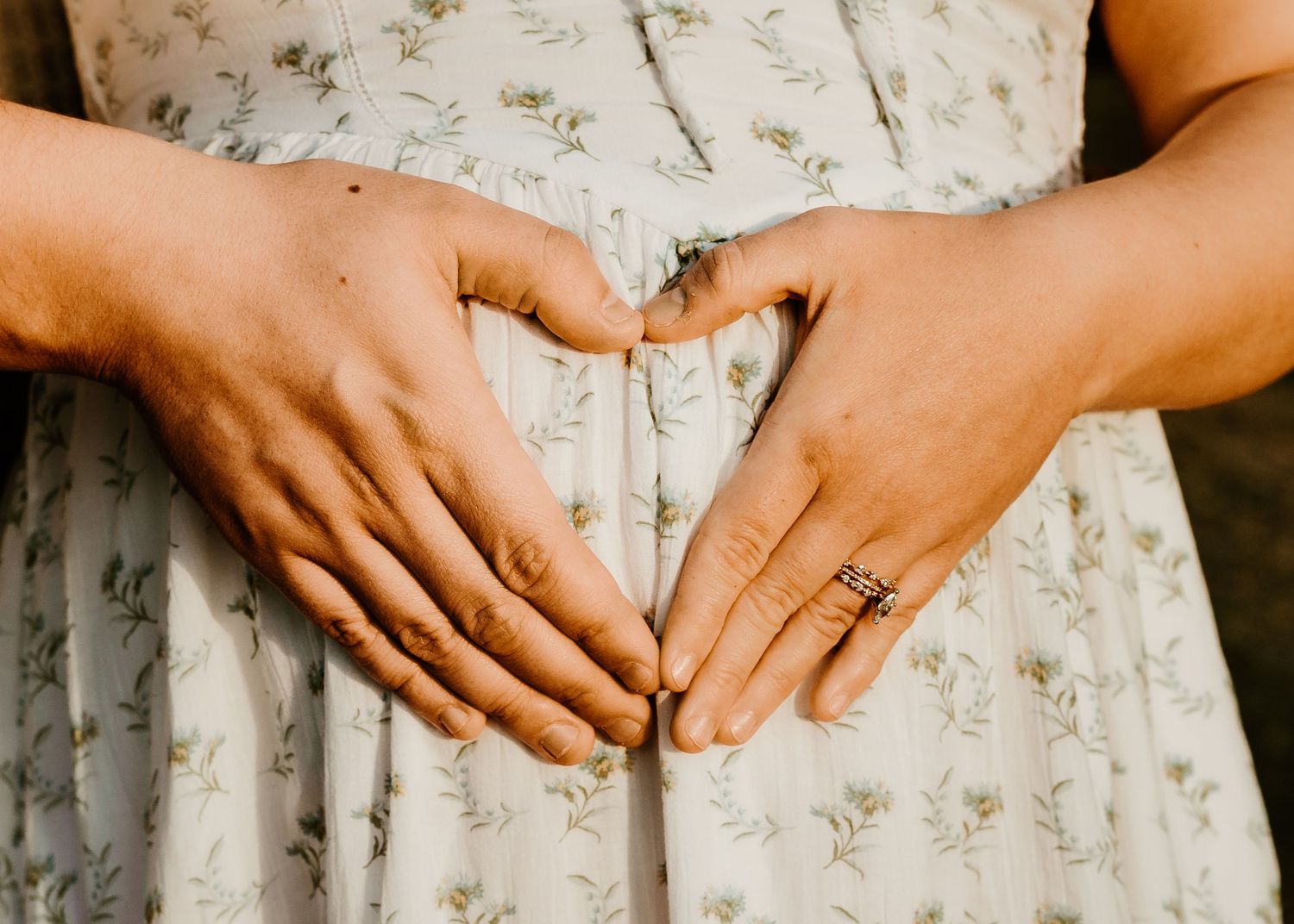 Close-up of hands forming a heart shape over a floral dress.