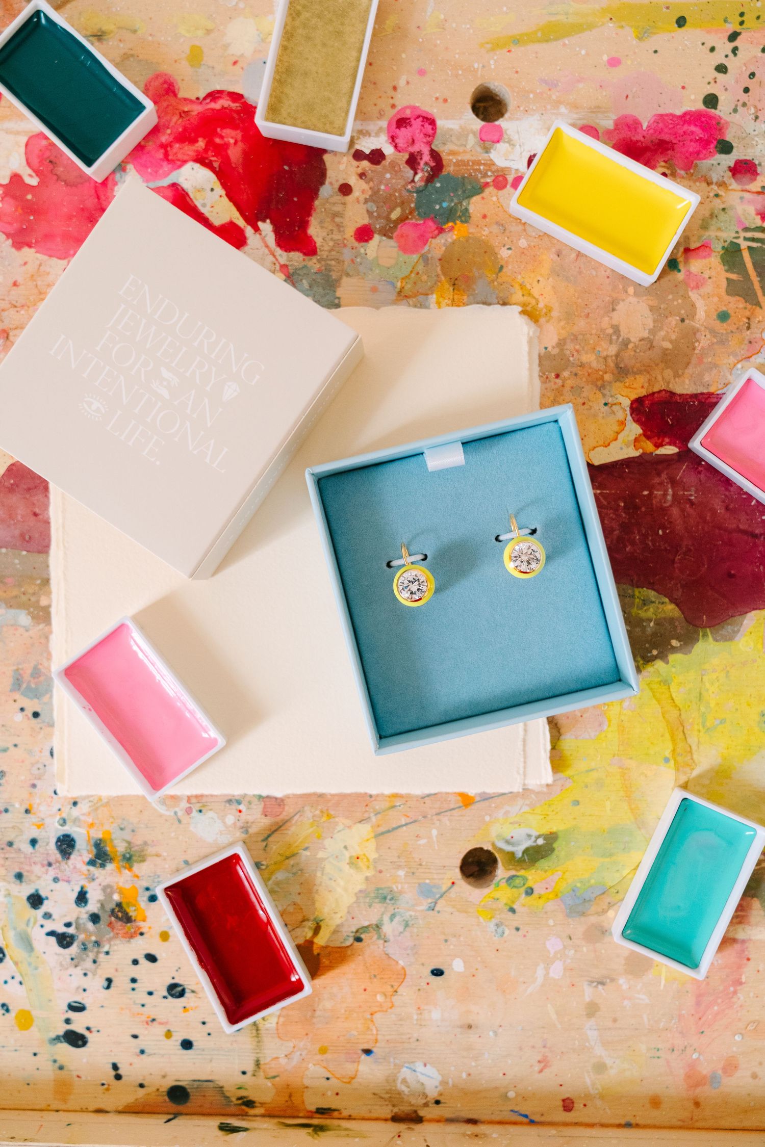 Artist's palette with vibrant shades of blue and turquoise paint being mixed with a paintbrush on white surface.