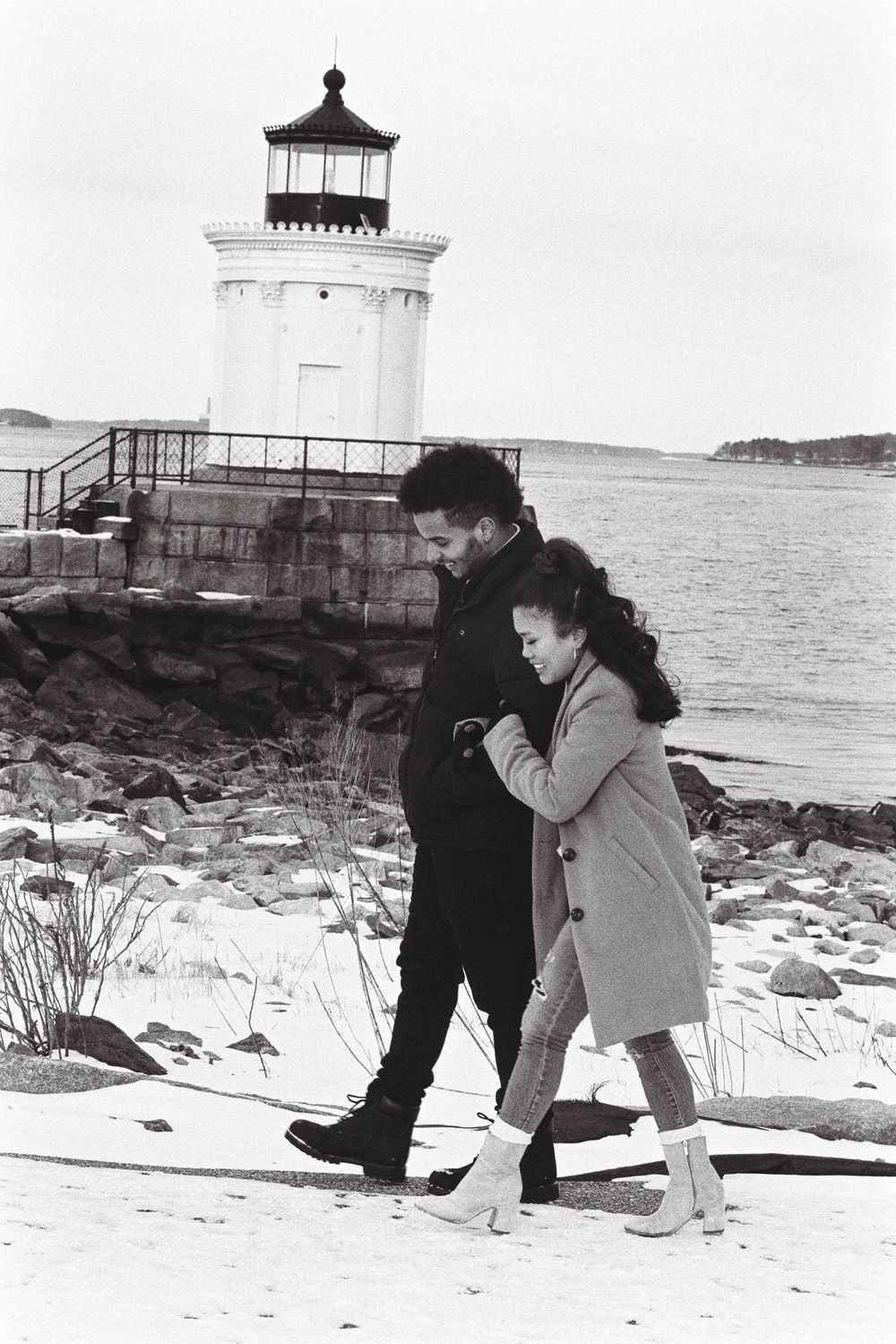 Recently engaged in the winter near a lighthouse in South Portland, Maine, this couple hold onto each other as they walk through the snow.