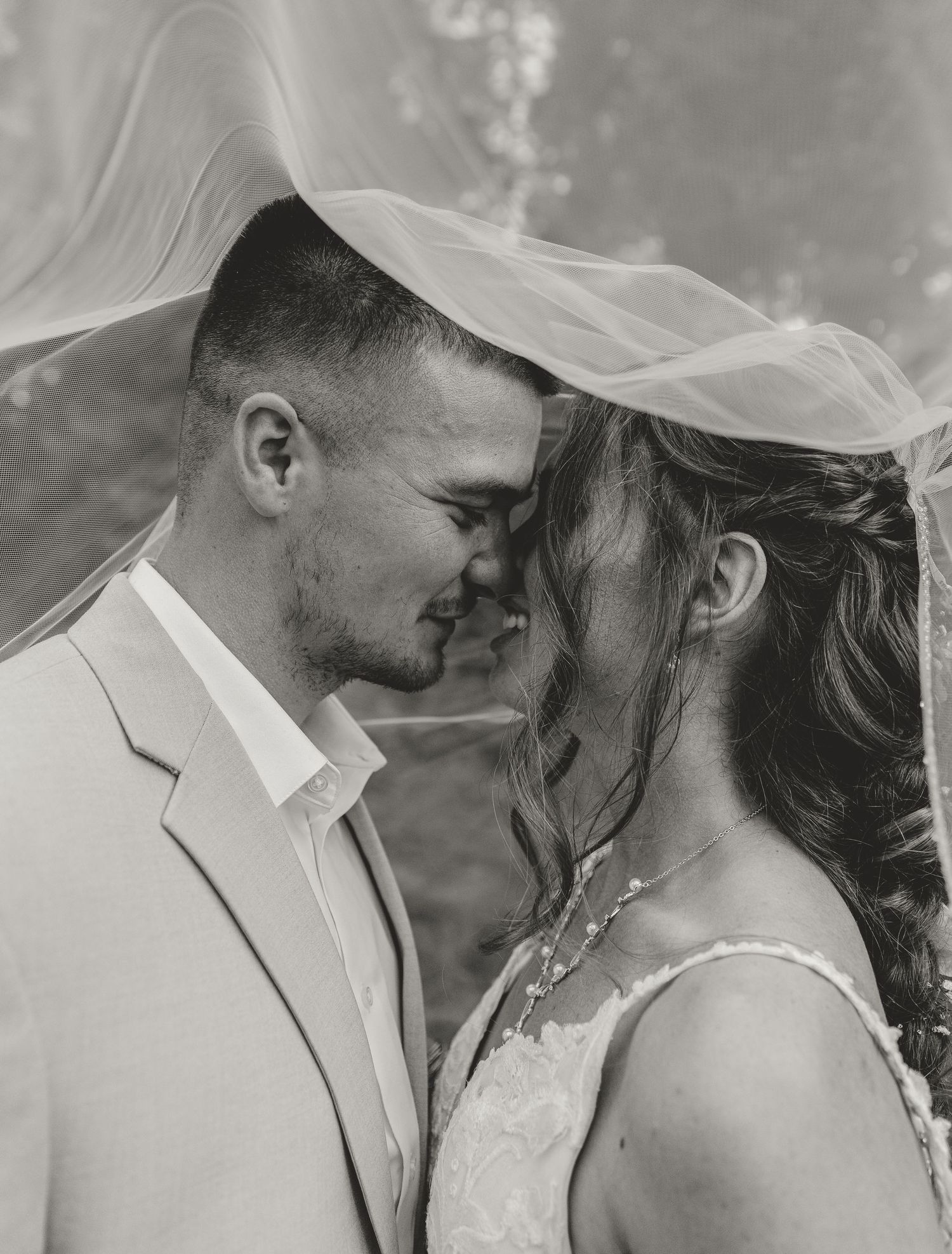 A romantic black and white wedding photo showing a tender intimate moment between newlyweds under a delicate veil.
