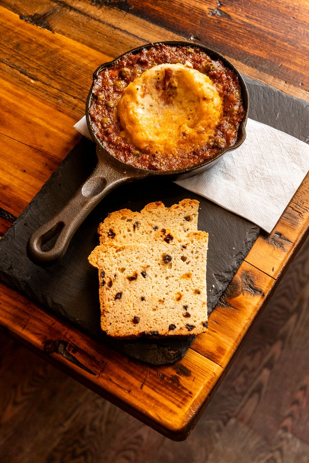 Fresh-baked bread with raisins served on a wooden cutting board with cast iron pan.