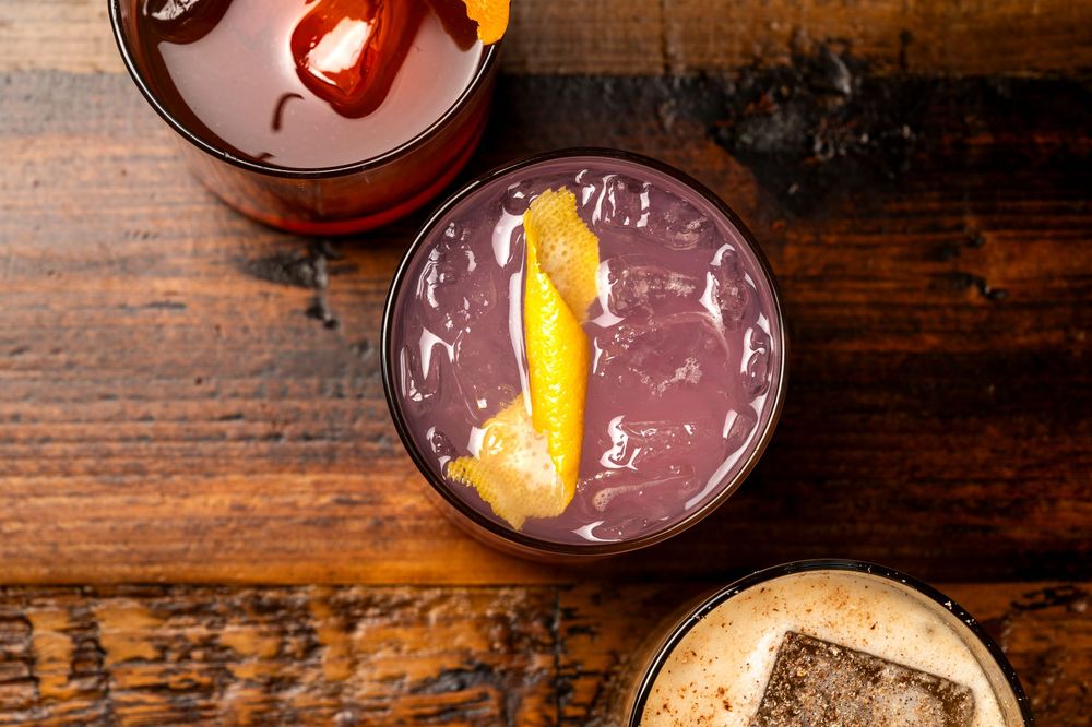 Row of colorful craft cocktails with citrus garnishes on a wooden bar.