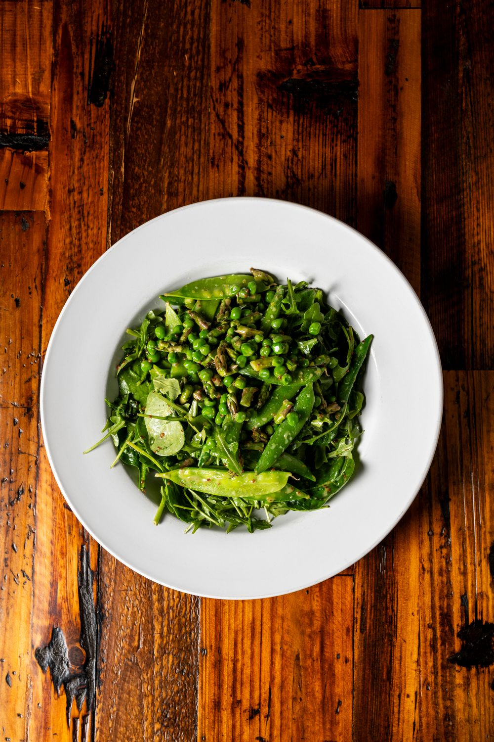 Fresh green salad with peas served on white plate against wooden table.