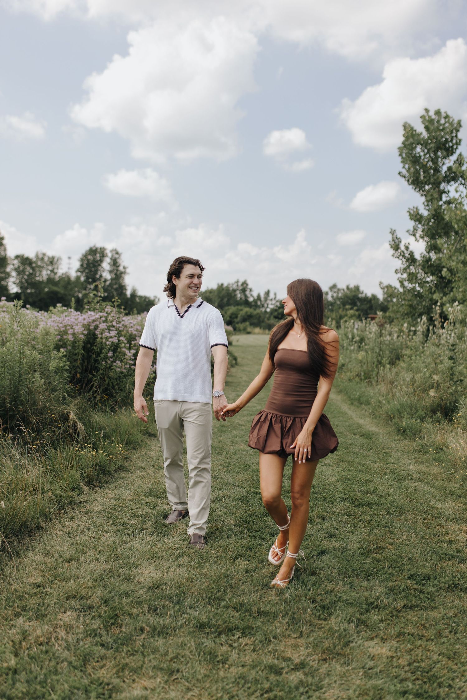 Engaged couple smiling and holding hands on a flower-lined trail at High Banks Metro Park.