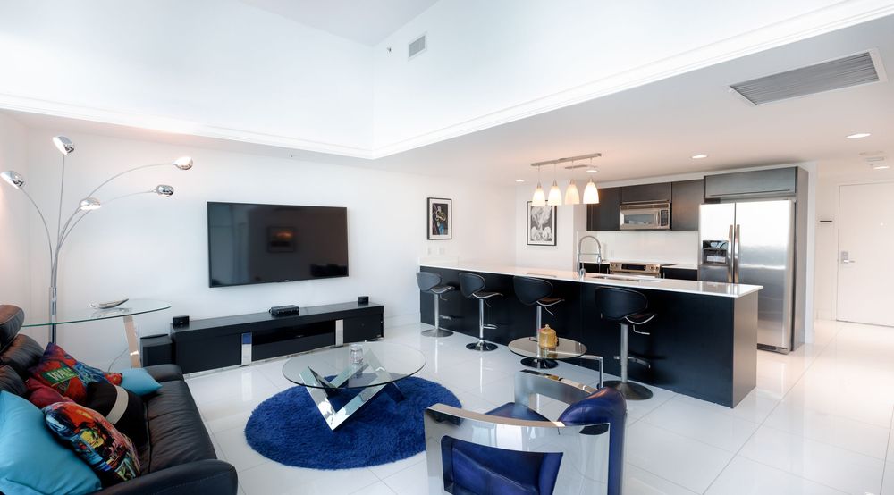 Modern open living area with black-and-white kitchen, breakfast bar seating, flat-screen TV, and stylish décor — Miami condo interior.