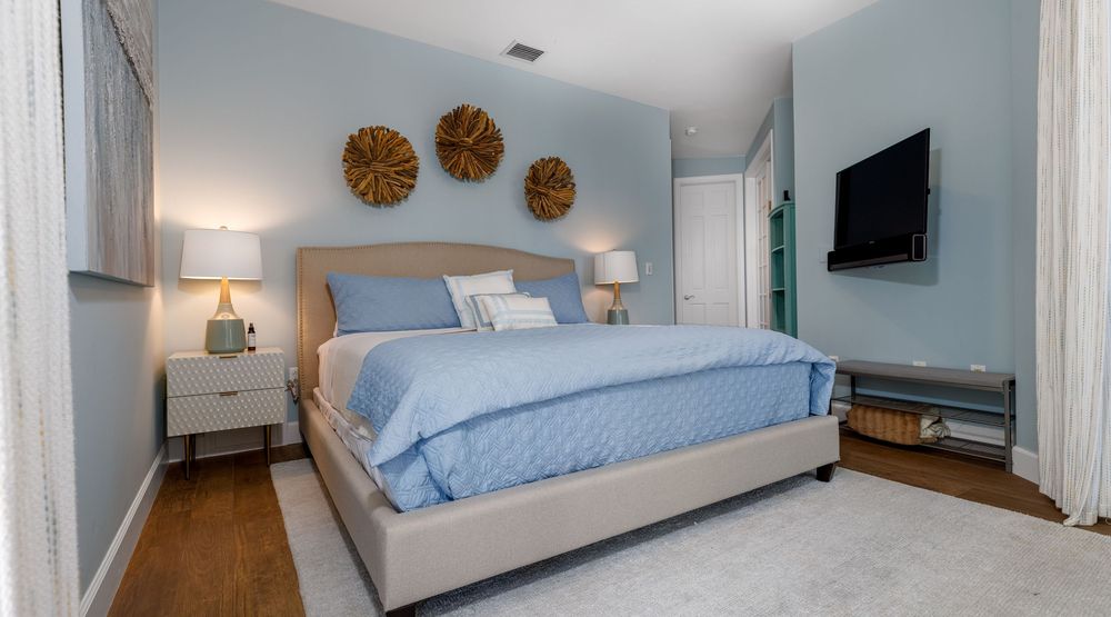Cozy primary bedroom with modern décor, blue accent walls, upholstered bed, hardwood floors, and wall-mounted TV — South Florida home interi