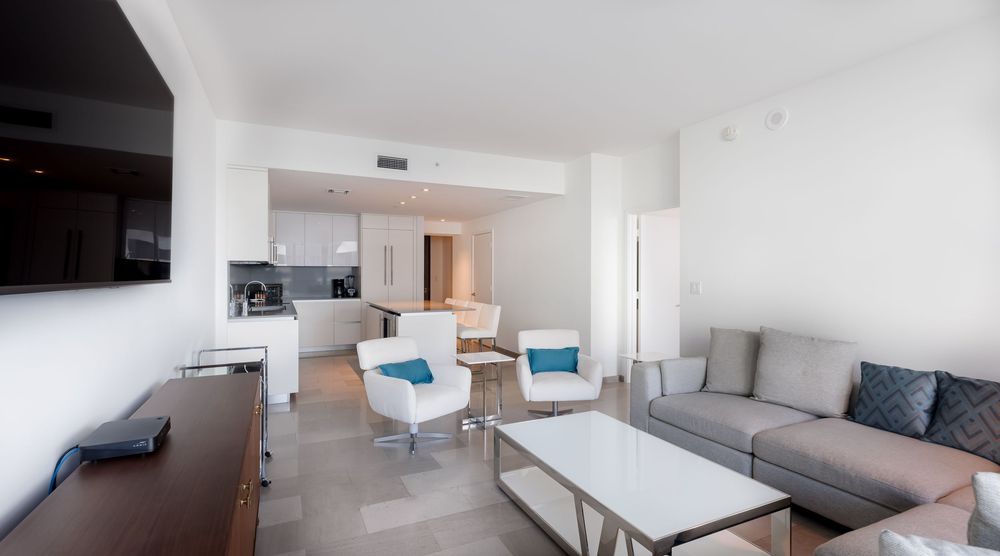 Modern open living space with neutral décor, sleek tile floors, contemporary furniture, and connected kitchen — Miami condo interior.