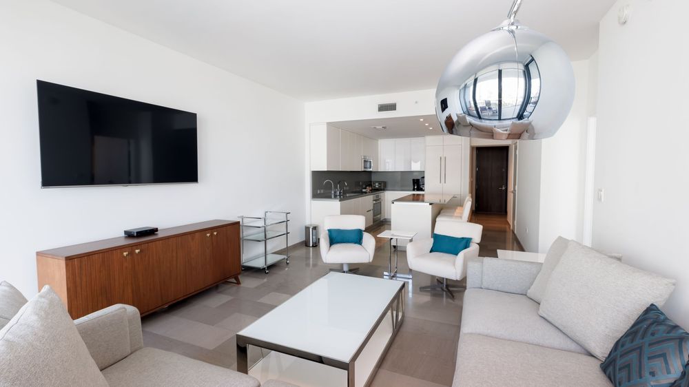 Contemporary living room with modern furniture, flat-screen TV, open kitchen layout, and stylish décor — Miami condo interior design.