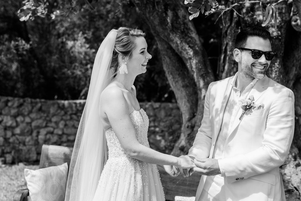 Ein Schwarz-Weiß-Foto einer Hochzeitszeremonie zeigt ein Paar, das sich während einer Feier im Garten im Freien an den Händen hält. Mallorca