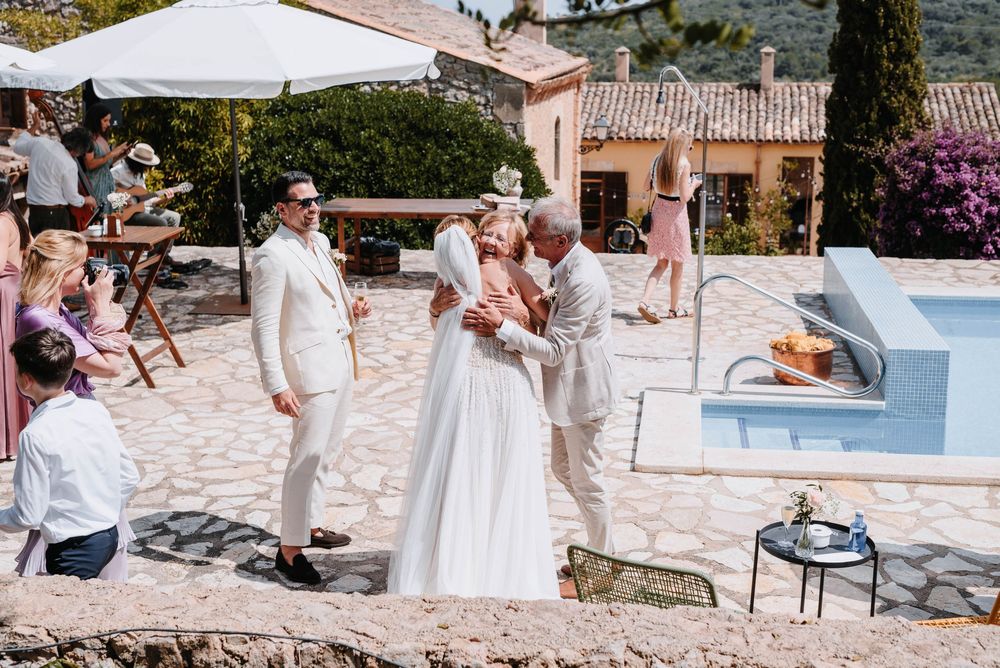 Sommerliche Hochzeitsfeier im Freien in einer mediterranen Villa mit Swimmingpool und weißen Sonnenschirmen an einem sonnigen Tag.