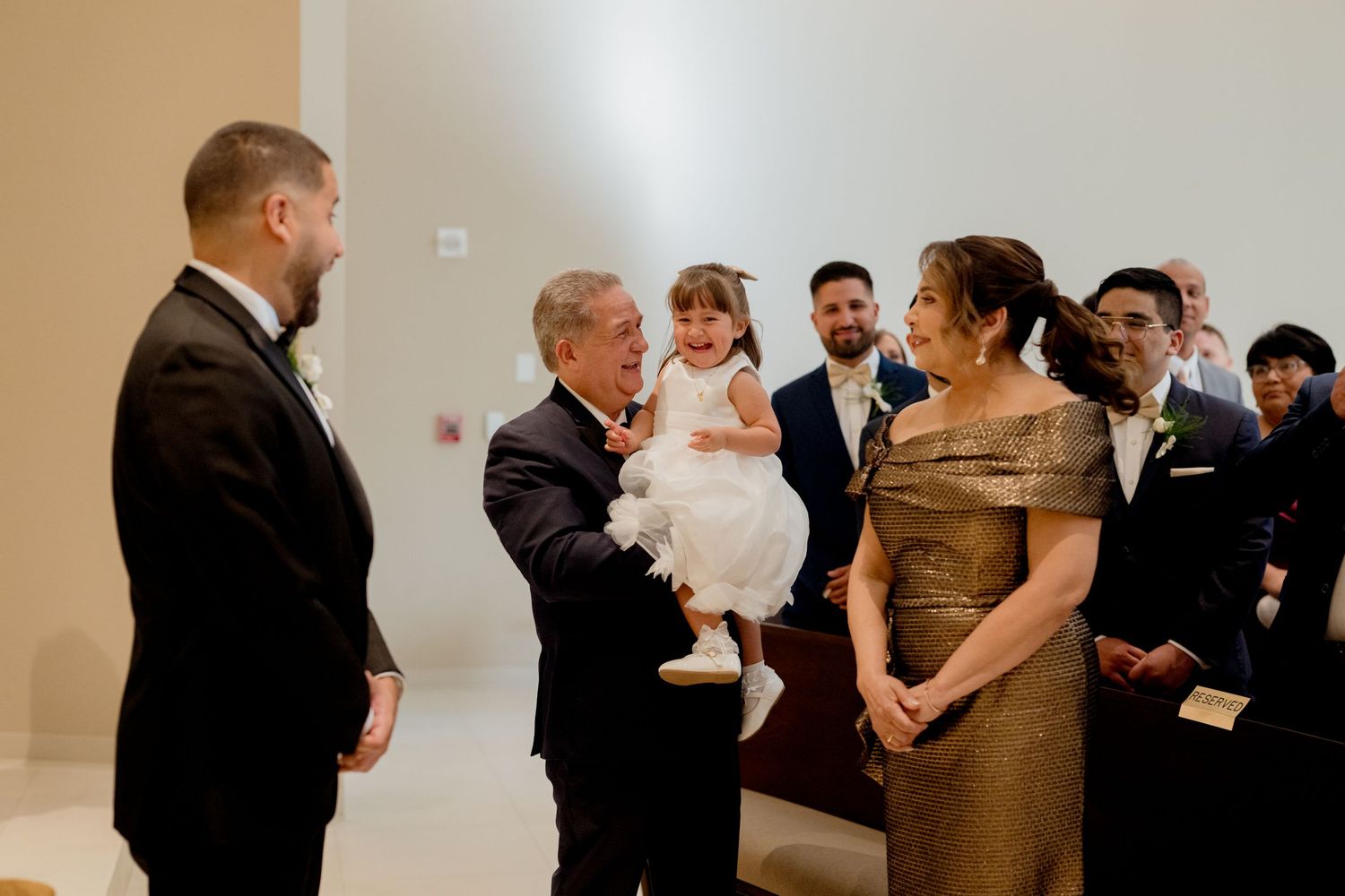 A group gathered in formal attire at an elegant indoor event, with a small child in a white dress.