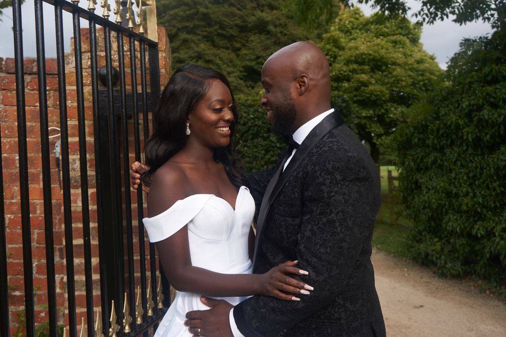A couple in formal attire embrace by a wrought iron gate during their wedding.