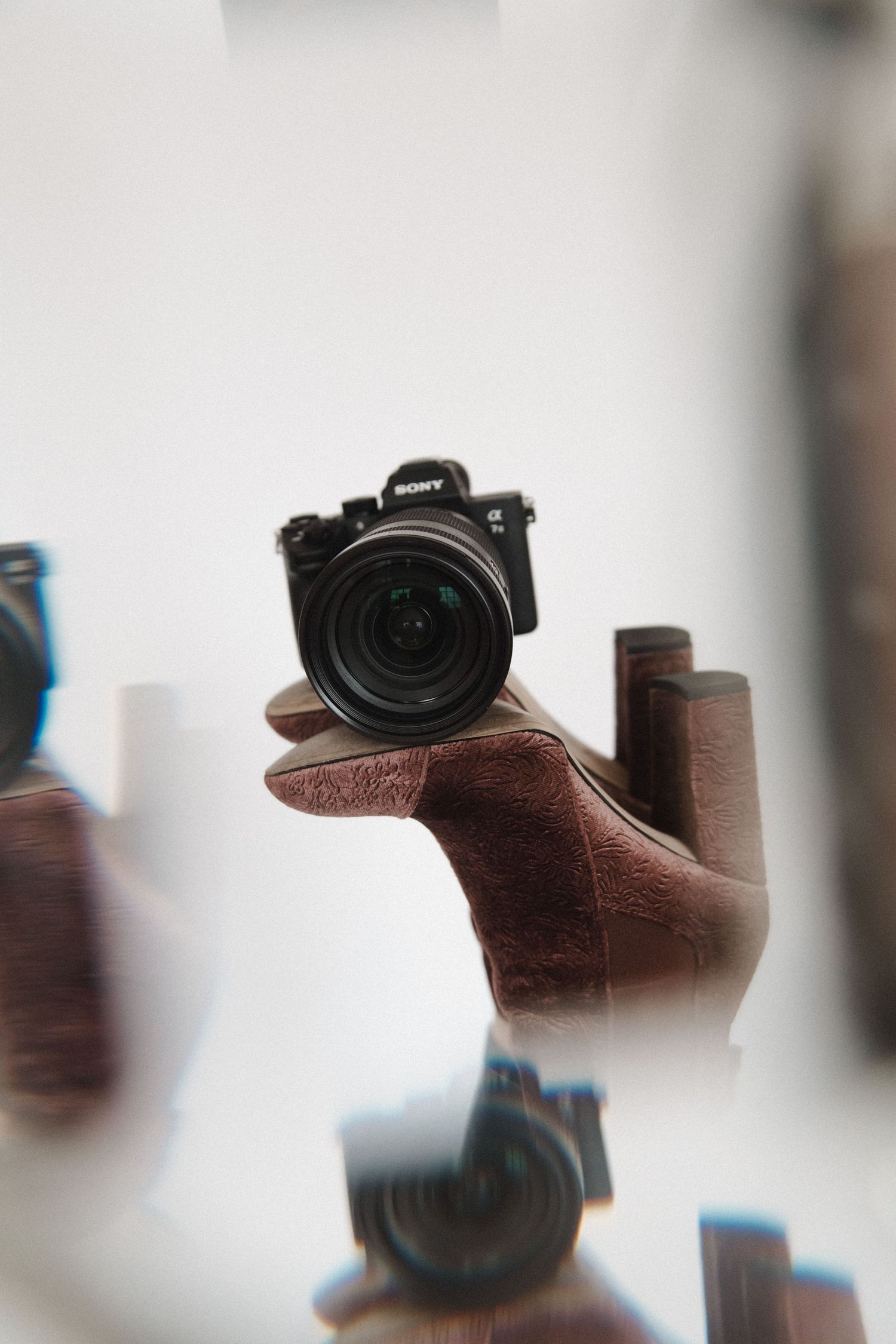 A mirror reflection creates a dreamlike double image of a camera sitting on a brown wooden surface.