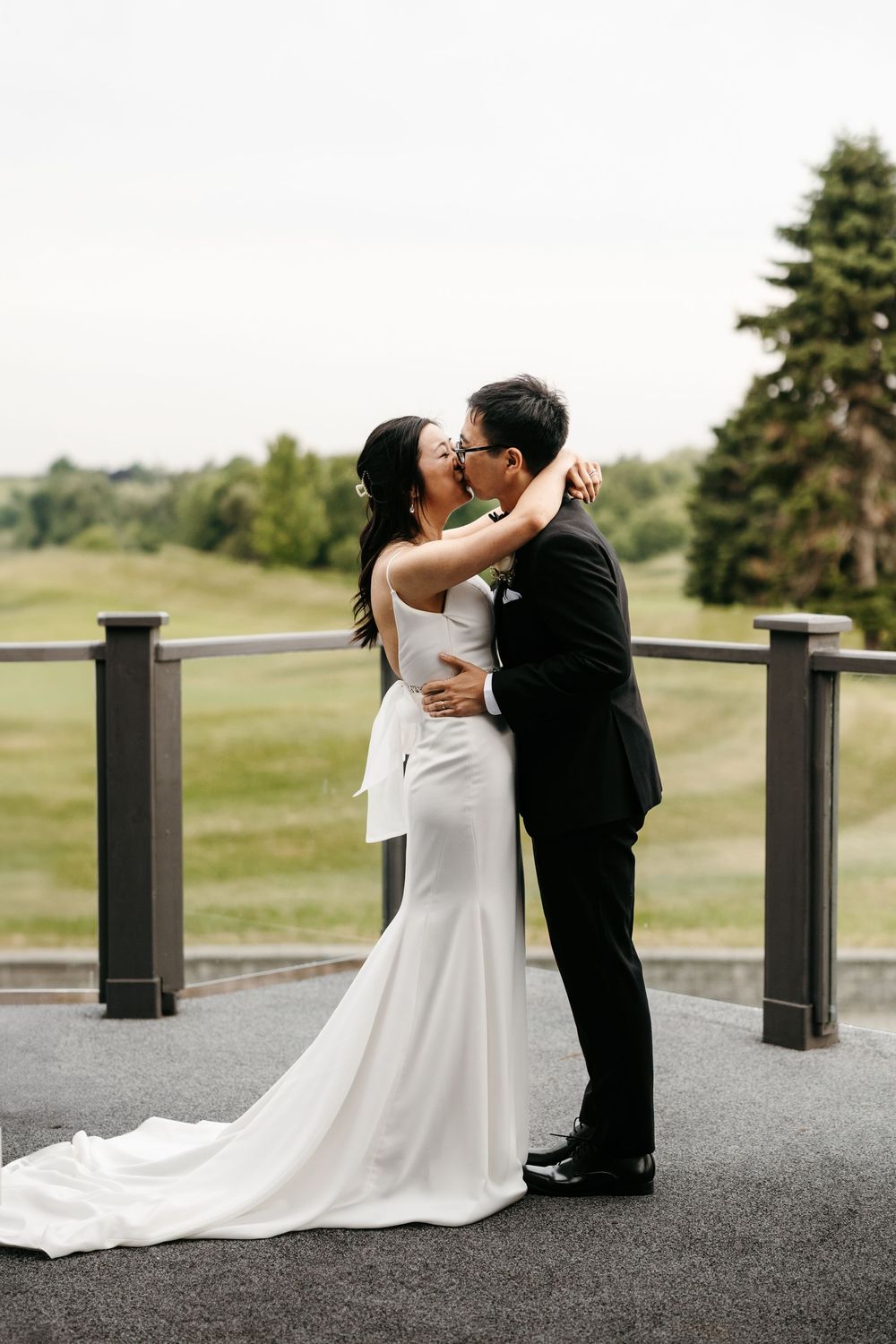 Couple sharing romantic kiss on outdoor terrace of golf course with scenic landscape in background.