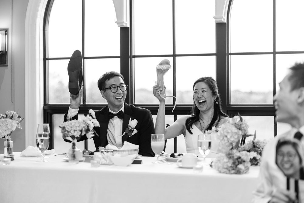 A joyful couple raises their hands in celebration while seated at an elegant black and white wedding reception.