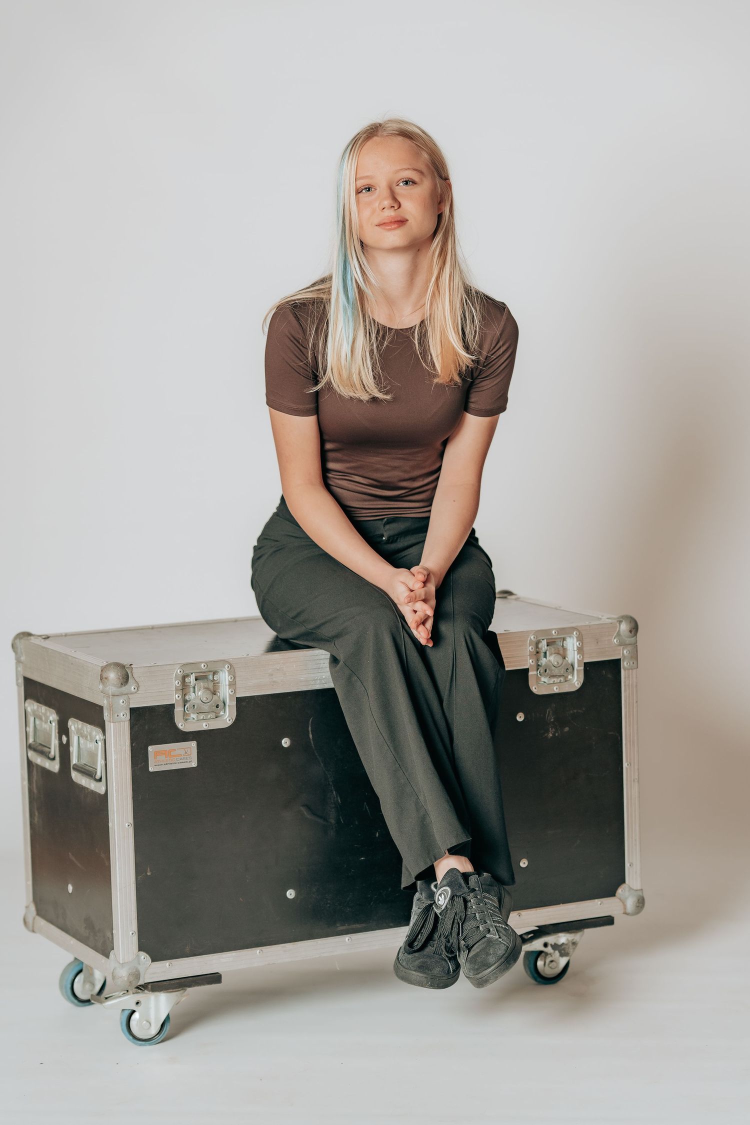 Studieportræt af en teenager siddende på en sort flightcase i et lyst fotostudie