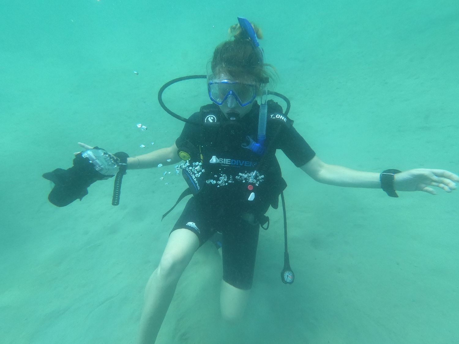A scuba diver in black wetsuit floats underwater in turquoise waters with arms outstretched.