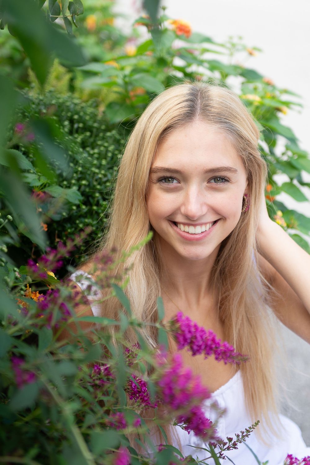 A bright portrait near vibrant purple flowers and greenery in a summer garden setting.