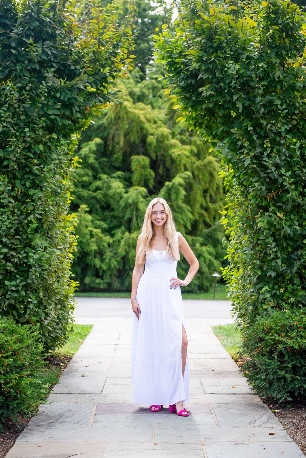 A series of outdoor portrait shots in a white dress along a garden pathway with green hedges and trees.