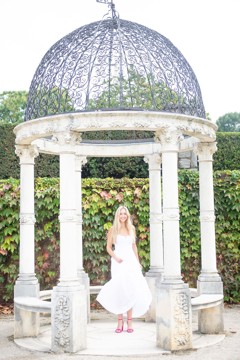 White gazebo structure with ornate columns and dome against garden backdrop with flowering vines.