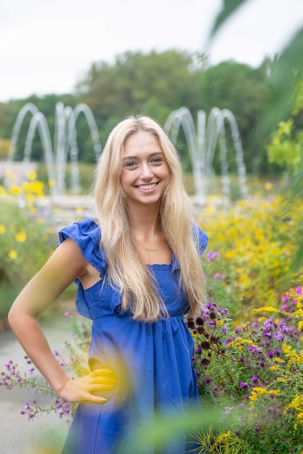 A blue summer dress stands out against a garden backdrop with yellow wildflowers and decorative fountains.