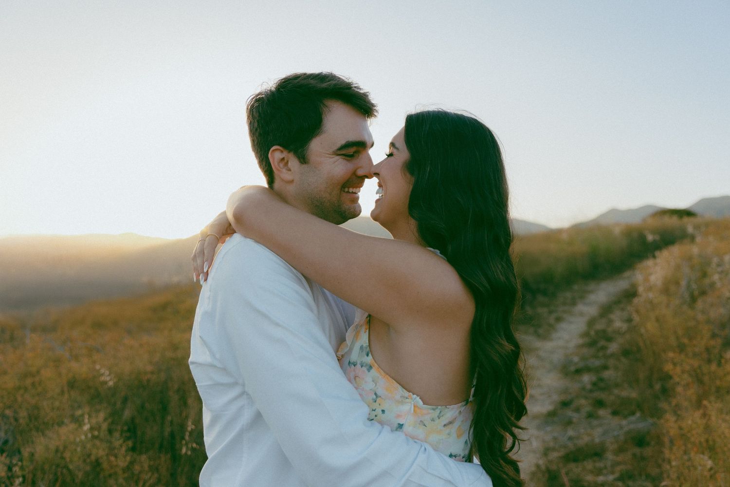 A couple embraces during sunset in a golden field with mountains in the background.