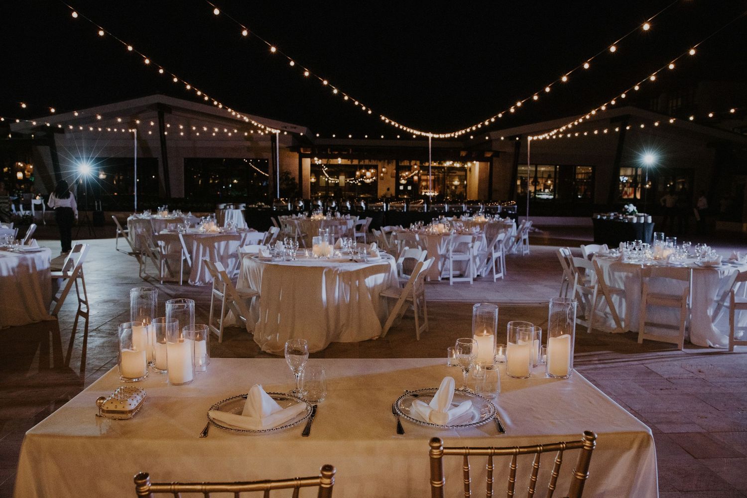 Wedding reception tables set under warm string lights creating a romantic evening ambiance.