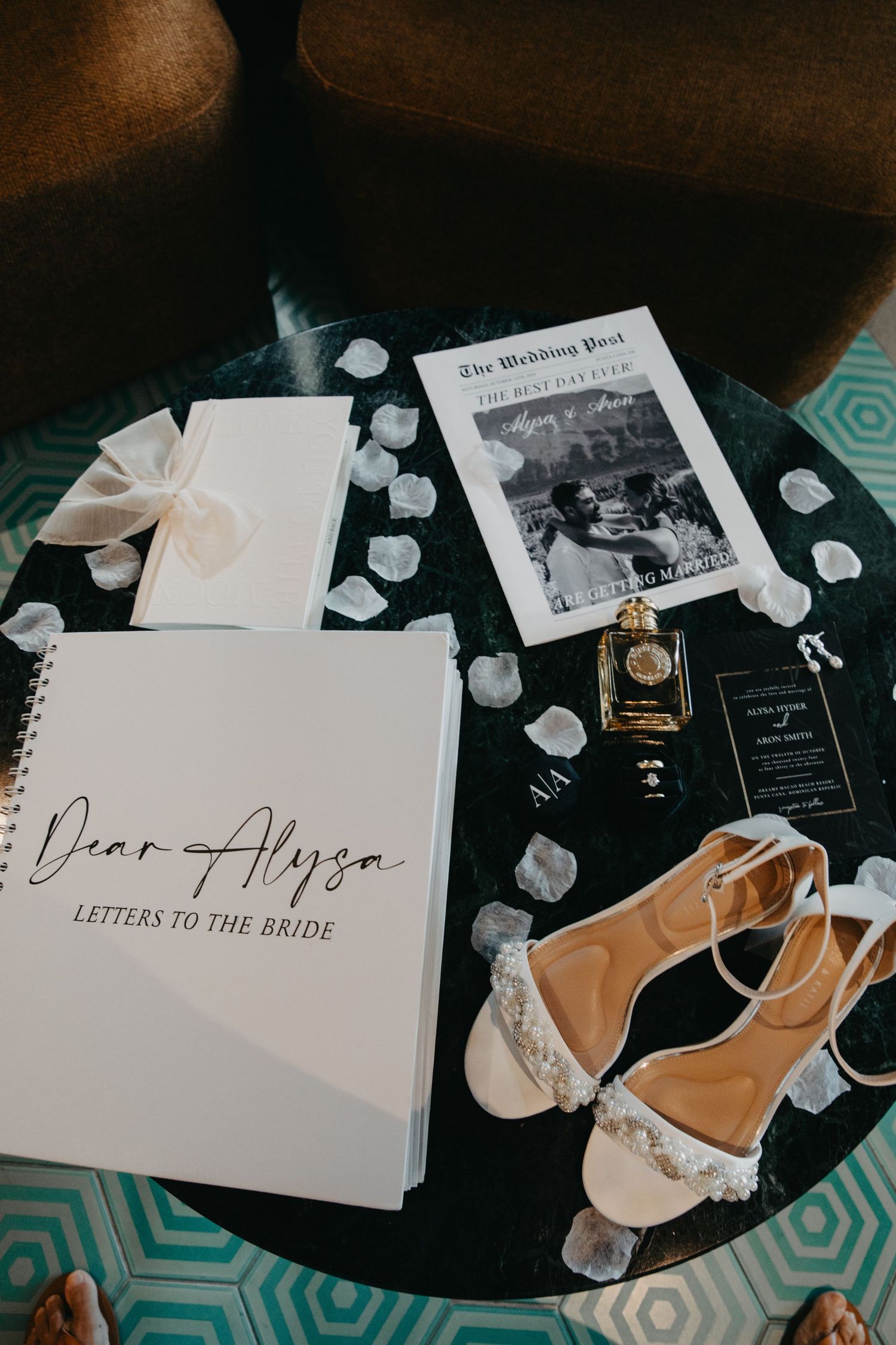 Wedding details including bridal shoes, letters to the bride book, and rose petals on a dark surface.
