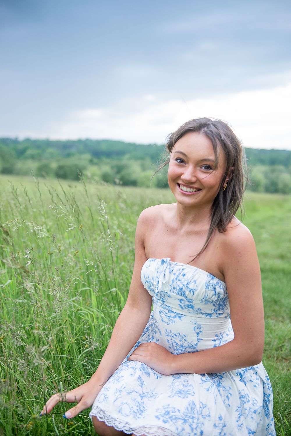 A person in a light blue and white strapless dress sits in a wildflower meadow on a summer day.