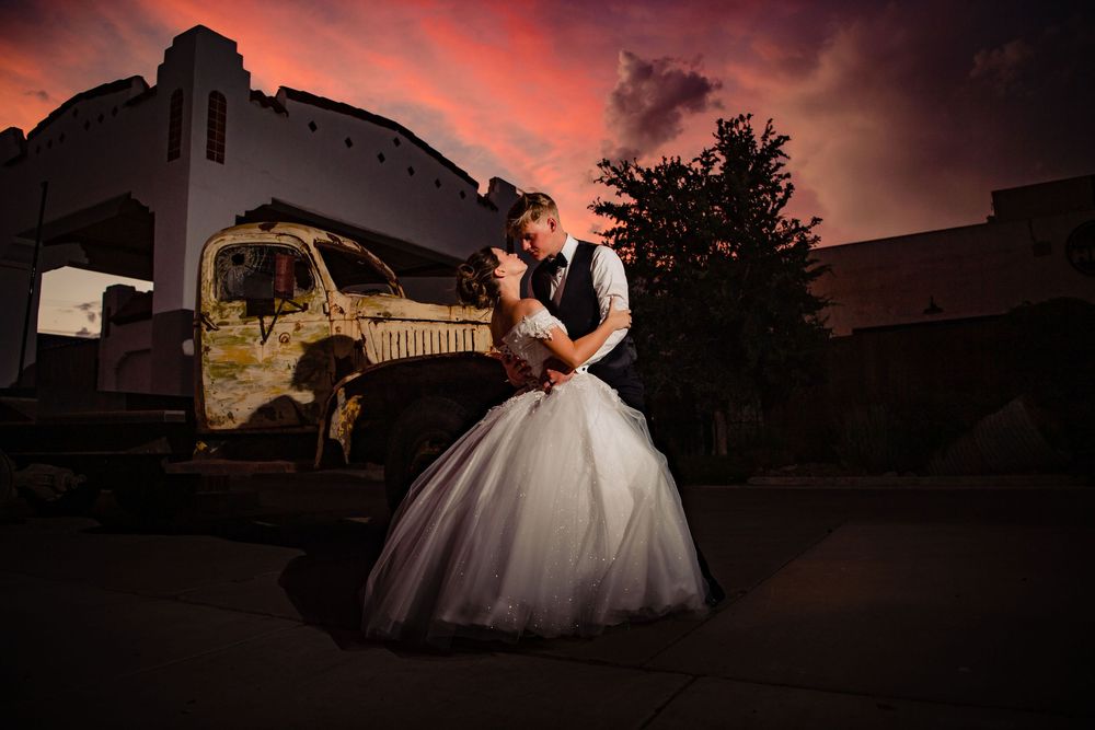 A couple embraces in front of an old train car during a dramatic sunset wedding photo shoot.