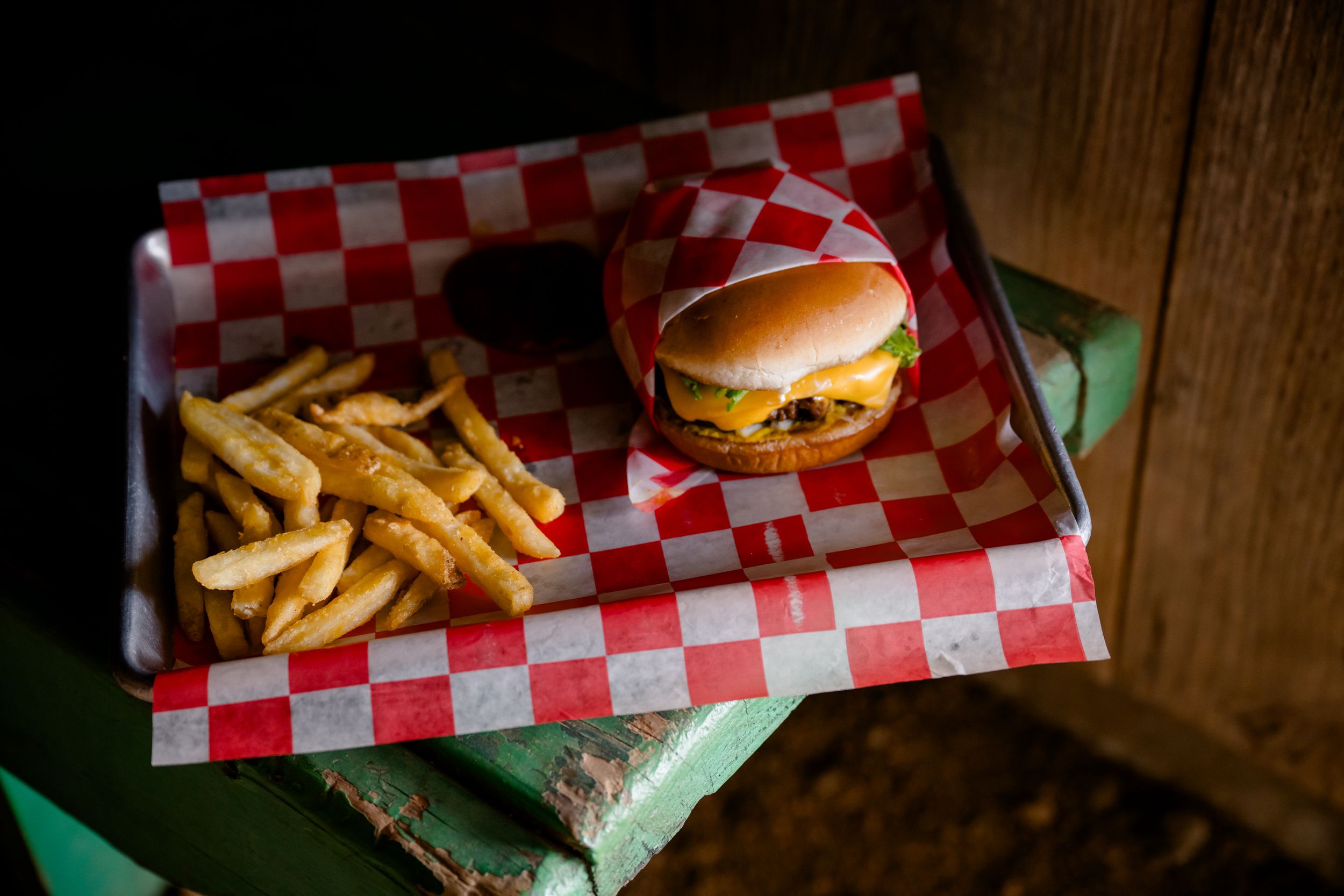 Delicious cheeseburger and crispy french fries served on red and white checkered paper in rustic wooden setting.