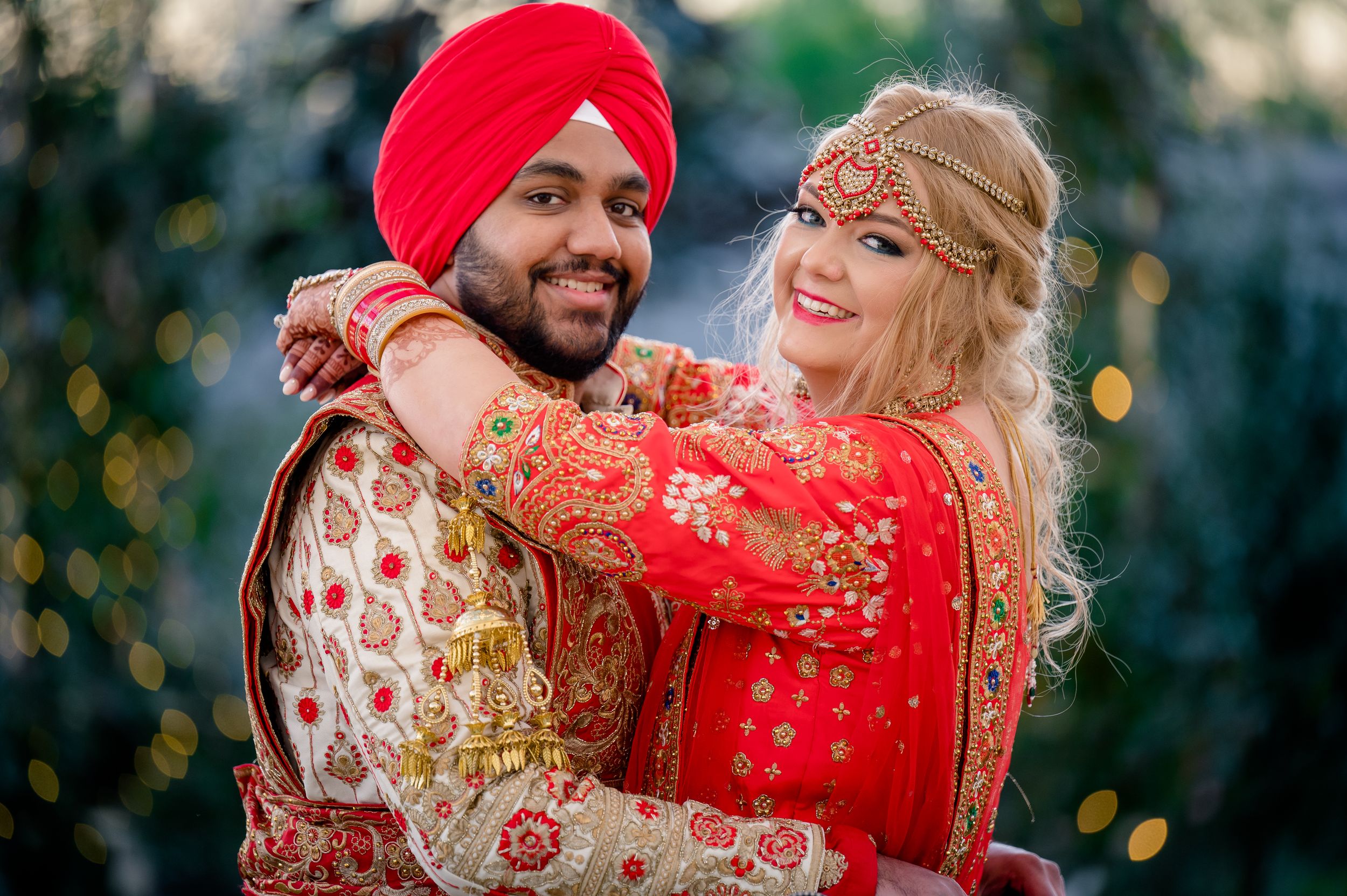 A festive outdoor photo session featuring traditional Punjabi wedding attire with vibrant red and gold colors.