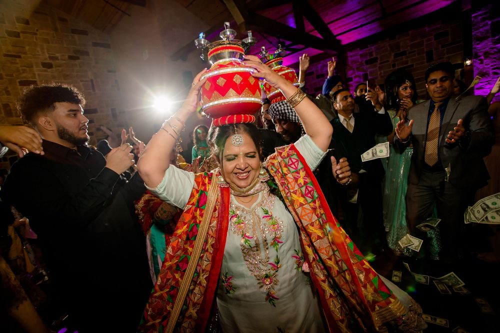 A bride in traditional red and gold Indian wedding attire dances under purple lighting during a celebration.