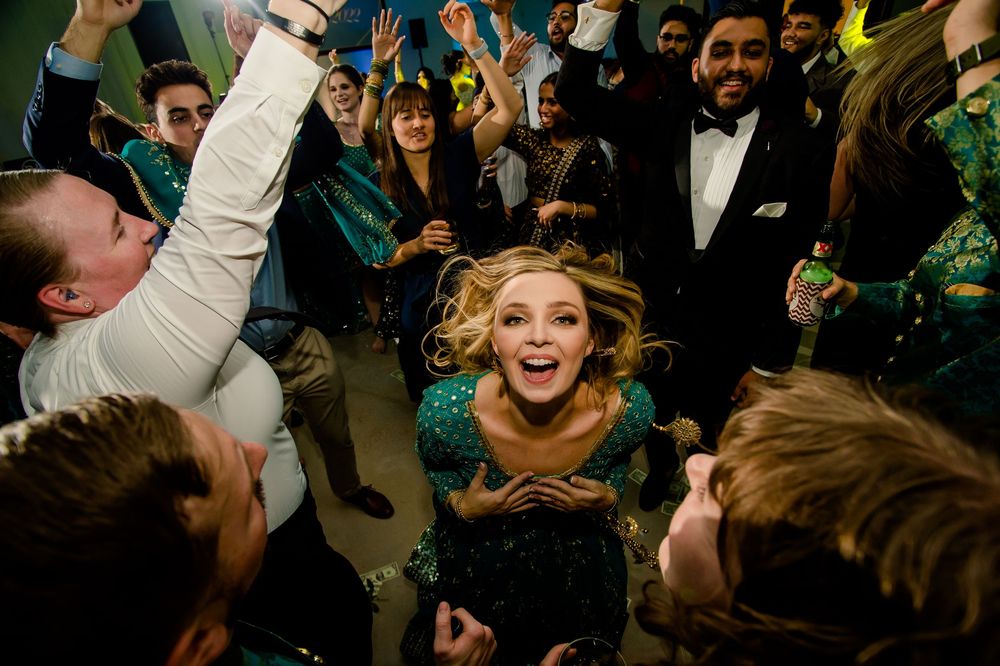 Joyful celebration scene at a wedding reception as party guests dance enthusiastically under green lighting.