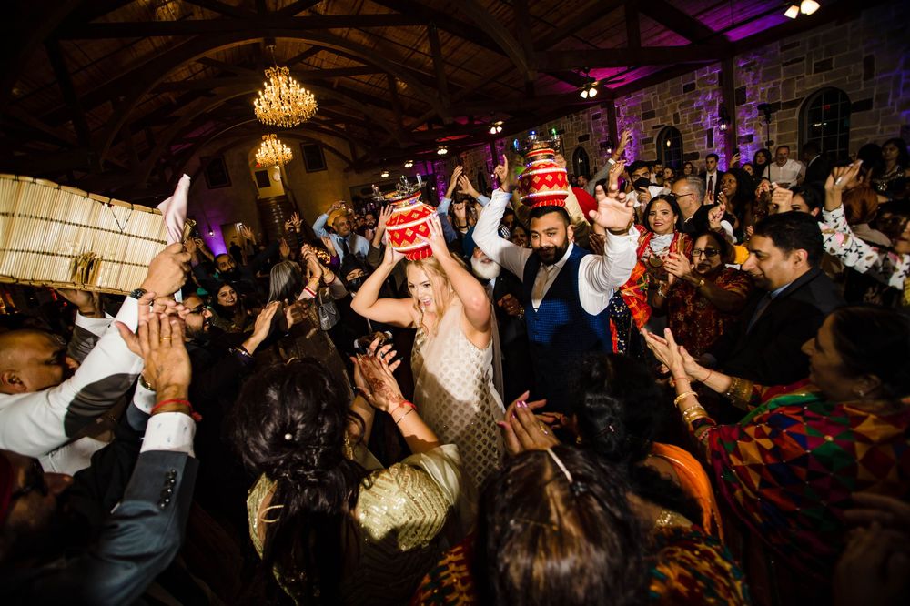 Large crowd of wedding guests dancing together on a dark dance floor with festive lighting and party atmosphere.
