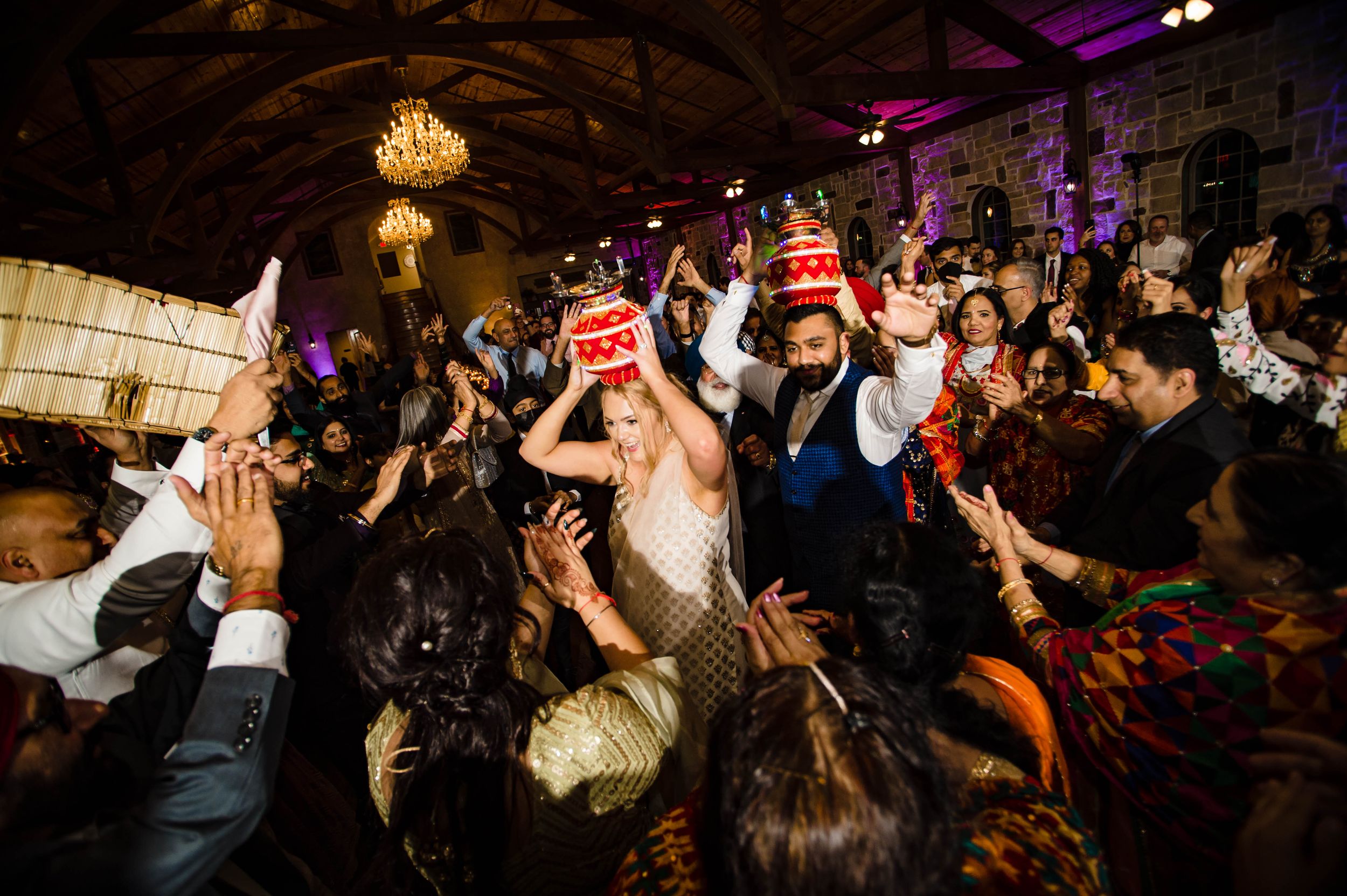 Large crowd of wedding guests dancing together on a dark dance floor with festive lighting and party atmosphere.