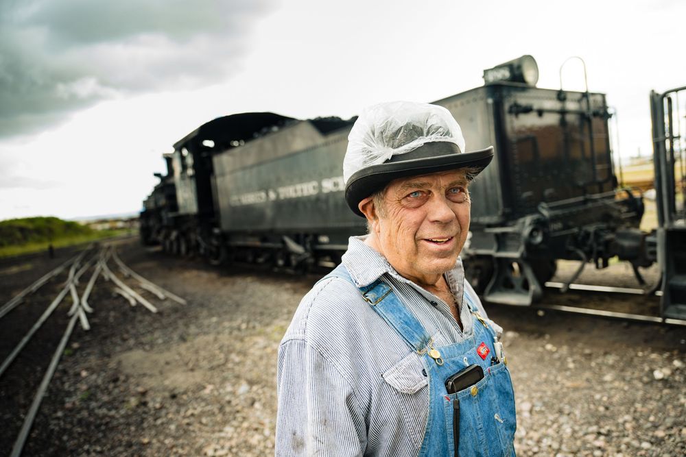 A series of vintage train cars and locomotives lined up on railroad tracks in a historical setting.