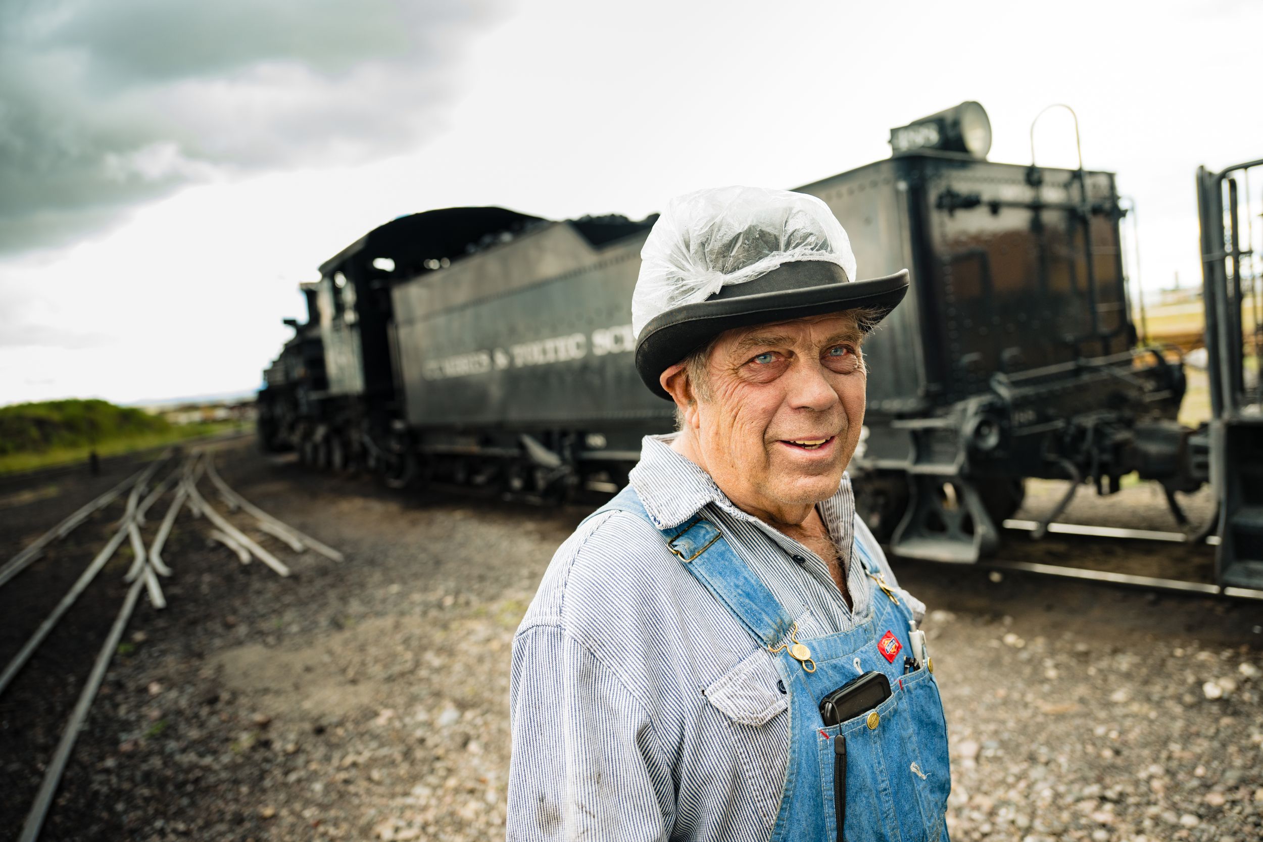 A series of vintage train cars and locomotives lined up on railroad tracks in a historical setting.