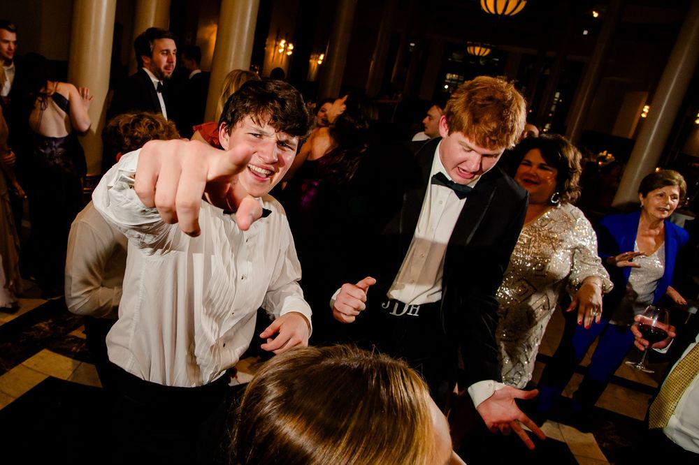 Energetic party guests dancing enthusiastically at a formal evening event with ambient lighting in the background.