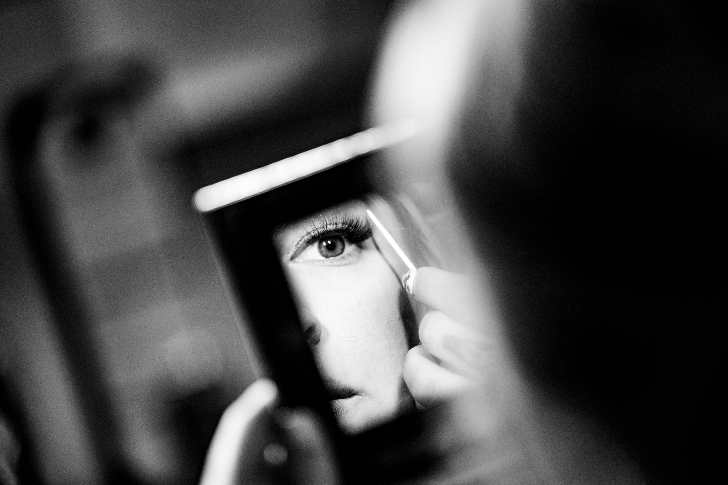 Black and white artistic photograph showing an eye with dramatic lighting and shadow through what appears to be a mirror reflection.