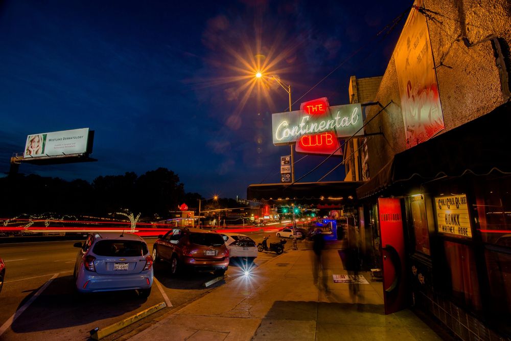 Panoramic nighttime view of a strip mall parking lot with glowing street lights and illuminated store signs.
