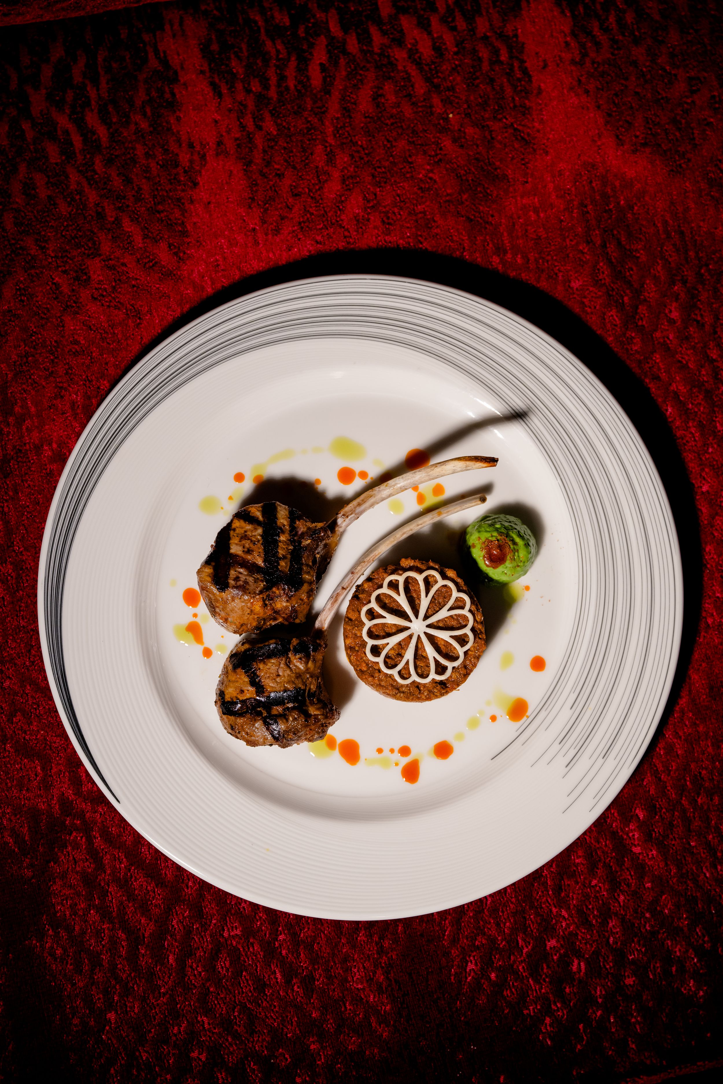 Elegant plated dish of seared meat with artistic sauce drizzles and garnishes on white plates against a deep red background.
